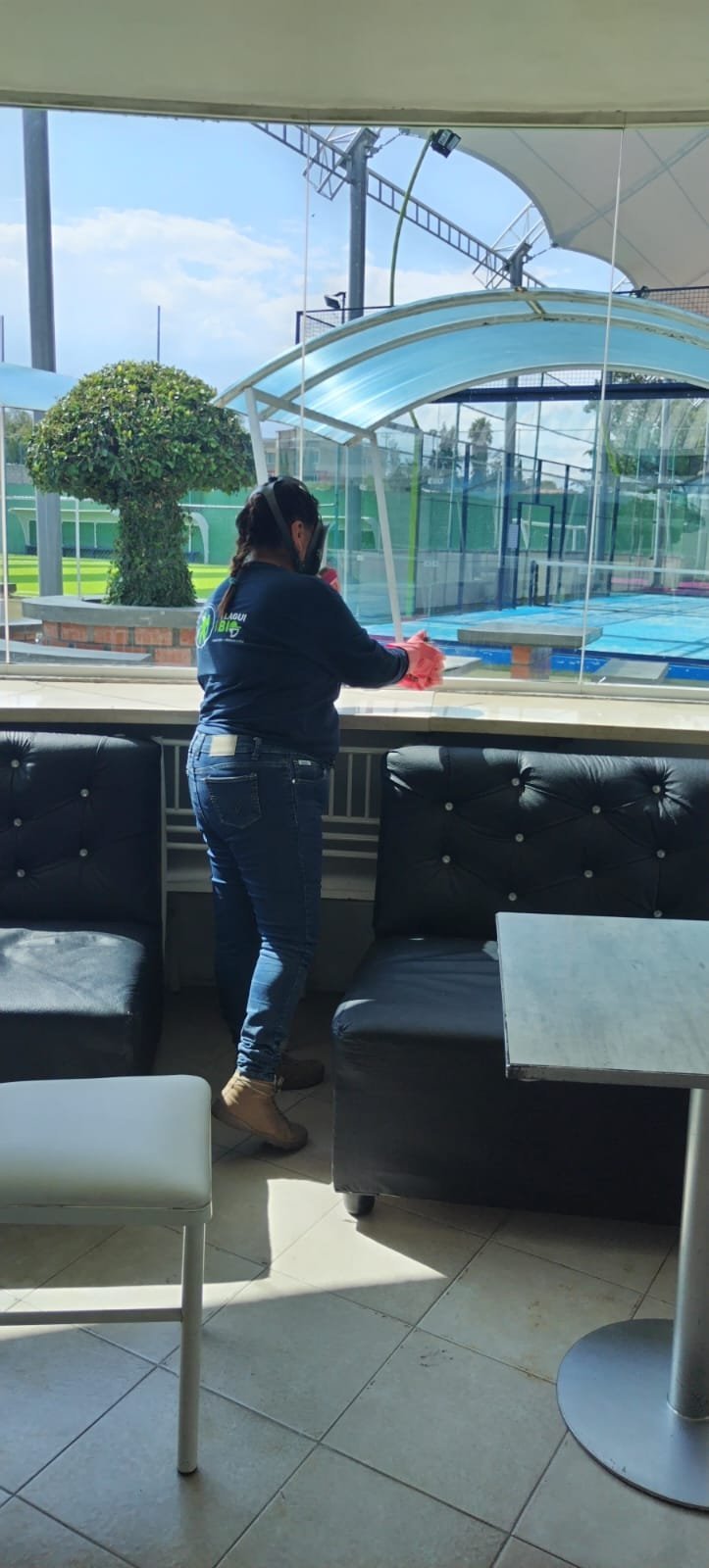Técnica PlaguiBio limpiando ventanas interiores en un club con vista a cancha de pádel